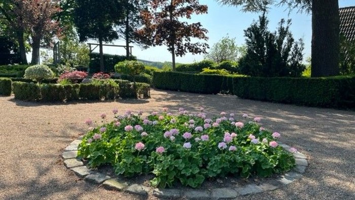 En smuk have med blomsterbænke og høje hegn.