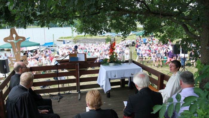Eine Gruppe von Menschen nimmt an einer Freiluftmesse teil, ein Priester steht am Altar.