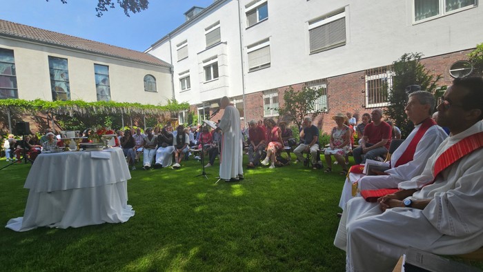 Priester und Gottesdienstbesucher sitzen im Kreis im GArten um einen Altar herum.