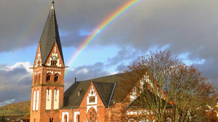 Eine auffällige Kirche mit einem hohen Kirchturm und einem lebendigen Regenbogen, der sich am Himmel dahinter wölbt.