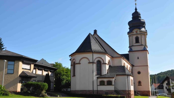Eine ruhige Kirche mit einem hohen Glockenturm und einem angrenzenden modernen Gebäude, umgeben von einer üppigen grünen Rasenfläche.