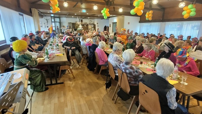 Ein festliches Treffen mit älteren Gästen in bunten Hüten, die ein gemeinsames Essen in einem geschmückten Saal genießen.
