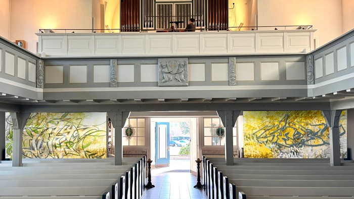 Elegante Kircheninnenausstattung mit Buntglas-Kunst, hölzernen Kirchenbänken und einer erhöhten Empore mit Orgel.