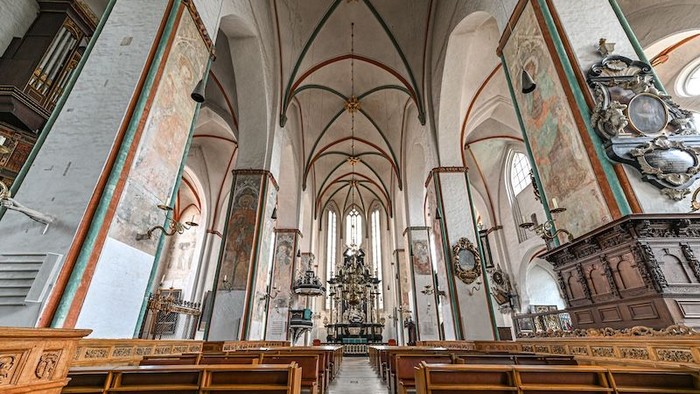 Historisches Kircheninneres mit hölzernen Kirchenbänken, prunkvollem Altar und imposanter gotischer Architektur mit detaillierten Verzierungen.