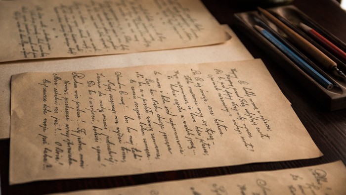Handschriftliche Notizen auf altem Papier, umgeben von Schreibutensilien auf einer dunklen Oberfläche.