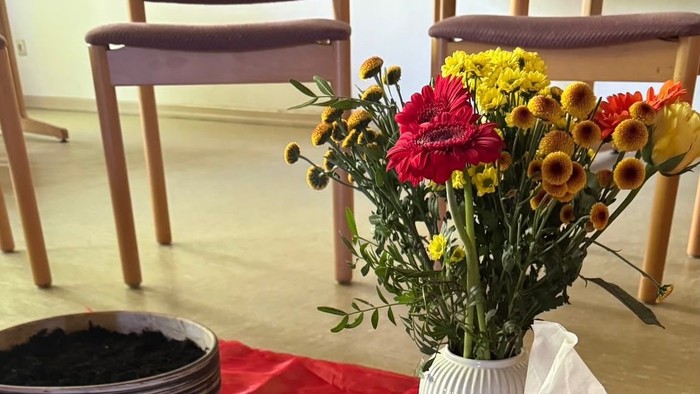 Veranstaltungseinladungstisch mit Datum, Handschuhen, Blumen und einem „Save the Date“-Schild für ein Gemeinschafts-Gedenkcafé.