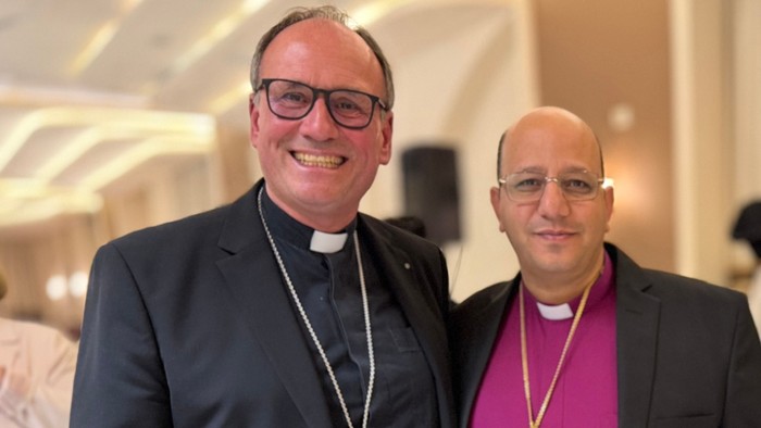 Zwei Geistliche in liturgischen Gewändern und Klerikerkragen, die gemeinsam mit Kreuzen posieren.