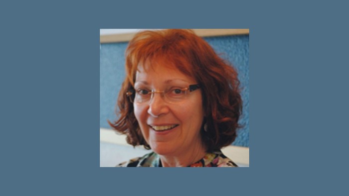 Eine Frau mit rotem Haar und Brille lächelt in die Kamera.