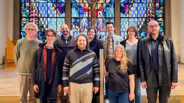 Neun Männer und Frauen lächeln in einer Kirche in die Kamera