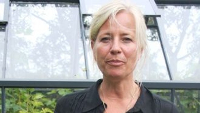 En kvinde i sort dress står i en drivhusmiljø.