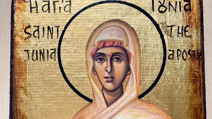 Eine traditionelle Ikone der Apostelin Junia auf goldenem Hintergrund. Die dargestellte Frau trägt ein helles Gewand mit Schleier und hält ein Kreuz in der Hand. Über ihrem Kopf befindet sich ein Heiligenschein. 