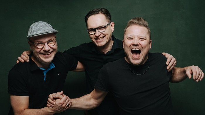 Ein Bild der Band Salesvuo Syncopation: Drei Männer halten sich die Hände und rufen etwas in die Kamera