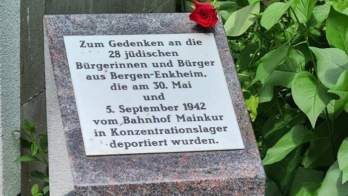 Gedenkstein aus dunklem Granit mit eingravierter Tafel für die 28 jüdischen Bürgerinnen und Bürger aus Bergen‑Enkheim, die 1942 deportiert wurden. Vor dem Stein liegen rote Rosen.