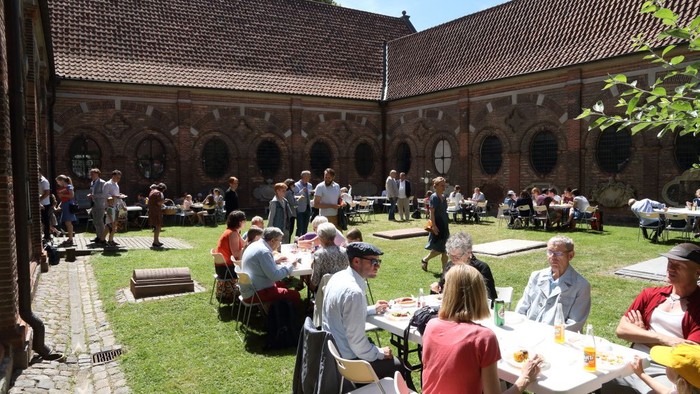 Die Leute versammeln sich im Freien auf einem Hof zu einer geselligen Veranstaltung mit Essen und Gesprächen.