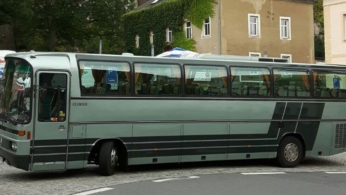 Ein grüner Reisebus fährt durch eine Stadt.