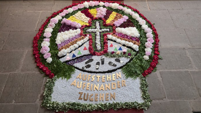 Bunter Blumen-Gedenkkranz mit Kreuz, Uhr und deutschem Text, der Einheit und Erinnerung symbolisiert.