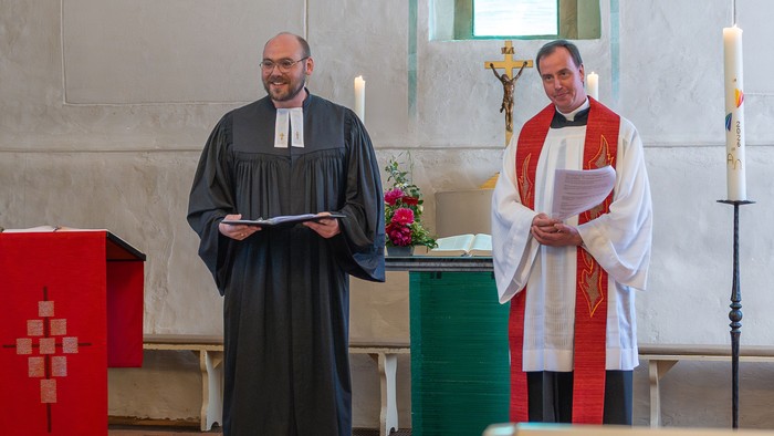Zwei Geistliche in Kirchengewändern stehen während eines Gottesdienstes an einem Pult.
