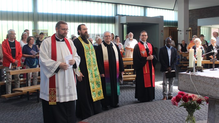 Religiöse Zeremonie mit Geistlichen, die einen Gottesdienst in einer modernen Kirche leiten, während Gemeindemitglieder sitzen und stehen.