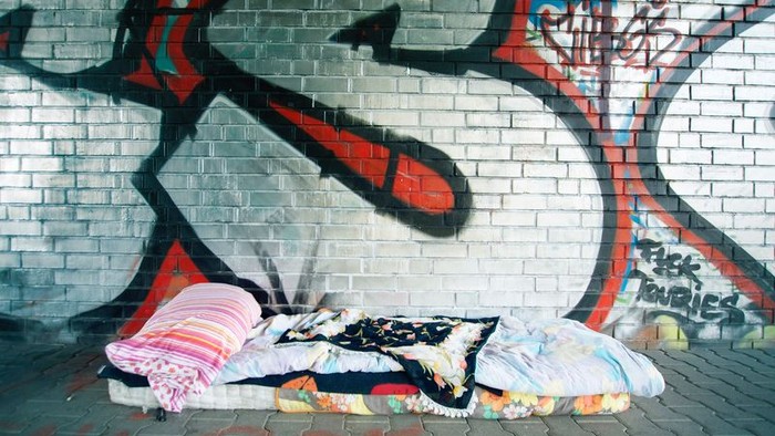 Ein Obdachloser schläft auf einer Decke vor einem Graffiti-Wand.