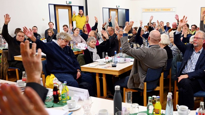 Gruppe von Menschen, die begeistert die Hände heben während eines Meetings oder Workshops mit Tischen voller Getränke und Notizen.
