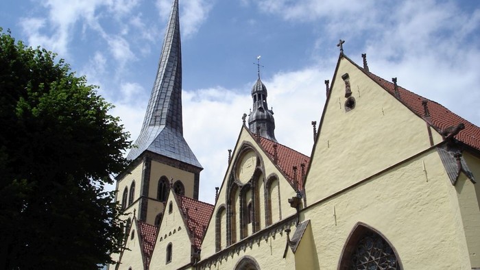 Historische Kirche mit hohem Turm und verzierter gelber Fassade unter einem teilweise bewölkten Himmel.