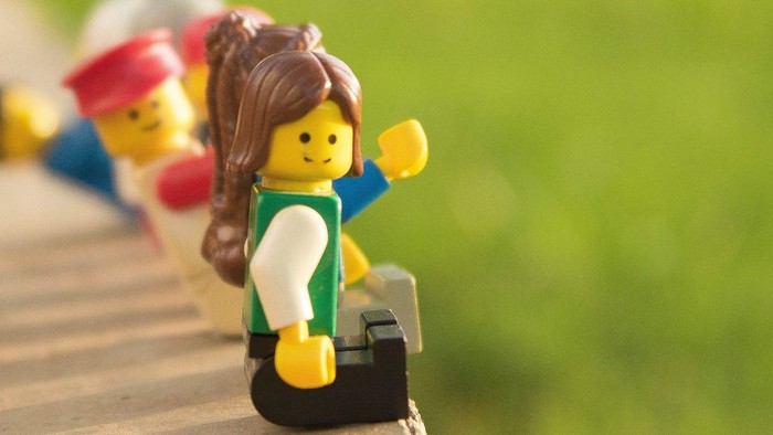 Kleine Lego-Figuren stehen auf einem Holzgeländer, eine hält einen Koffer.