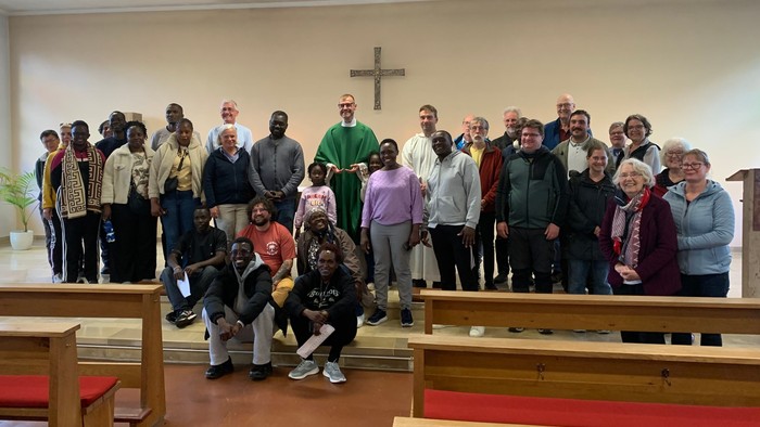 Gruppe verschiedener Menschen, die gemeinsam in einer Kirche mit Kirchenbänken und einem Kreuz posieren.