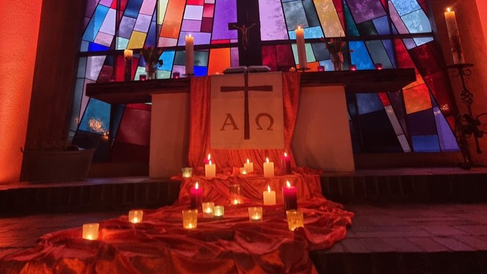 Buntes Glasfenster erleuchtet den mit Kerzen und einem Kreuzsymbol geschmückten Altar.