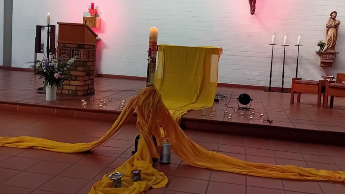Religiöser Altaraufbau mit gelbem Tuch, Kerzen und einer Kreuzigungsszene vor einer Ziegelsteinwand.