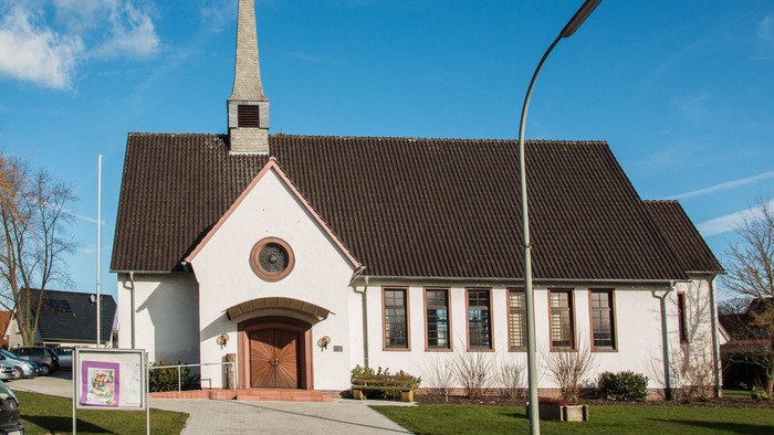 Weiße Kirche mit hohem Turm und schwarzem Dach unter blauem Himmel