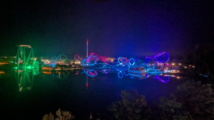Lebhafte nächtliche Fahrgeschäfte im Vergnügungspark spiegelten sich wunderschön im ruhigen Wasser darunter.