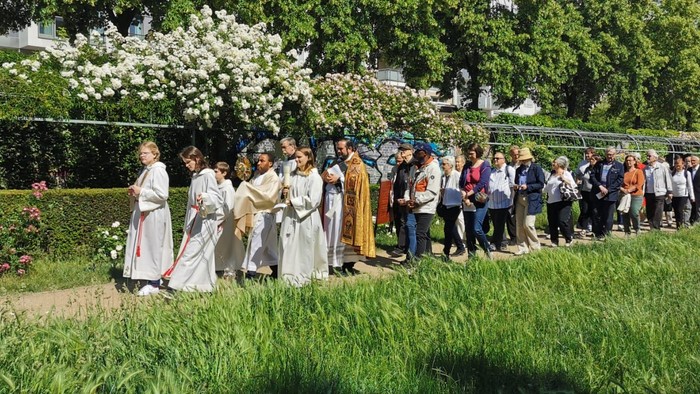 Eine vielfältige Gruppe steht in einem Garten, hält sich an den Händen in einer Reihe neben blühenden Bäumen und Grünpflanzen.