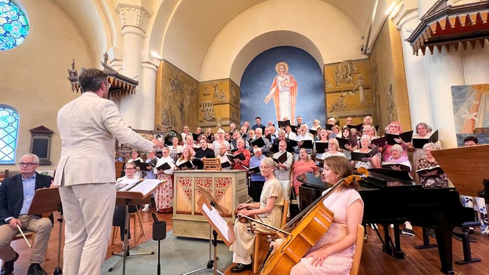 Ein gemischter Chor singt in einer Kirche mit vielen Wandmalereien