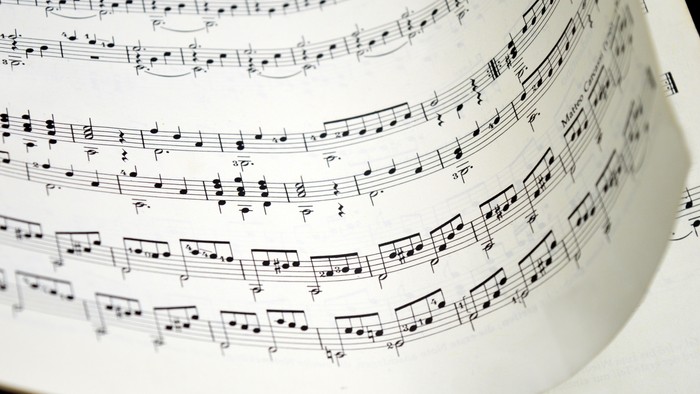 Notenblatt, das in einem gebogenen, zylindrischen Notenständer mit mehreren Notenzeilen musikalischer Notation dargestellt wird.