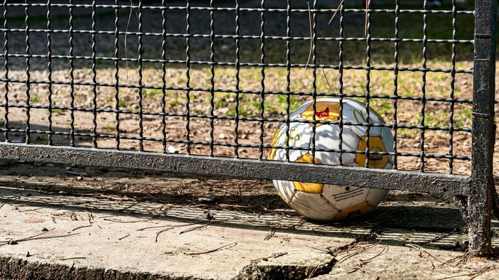 Ein Fußball liegt hinter einem Zaun