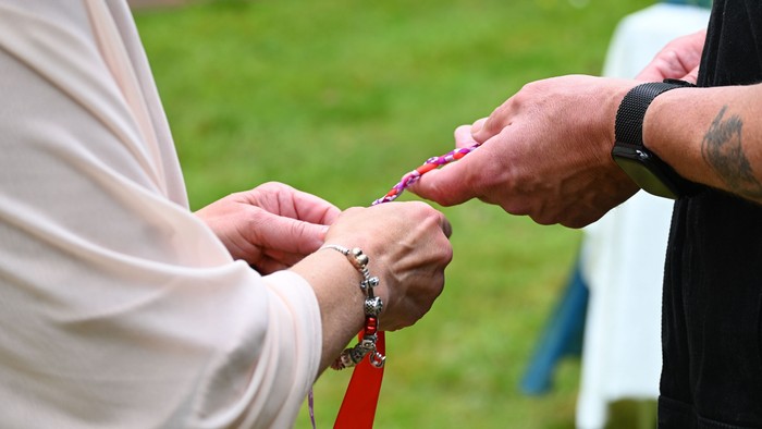 Ein Mann und eine Frau halten ein Segensband, ein aus bunten Bändern geflochtenes Band, in den Händen, das Teil einer Segenszeremonie für ihre Liebe ist.