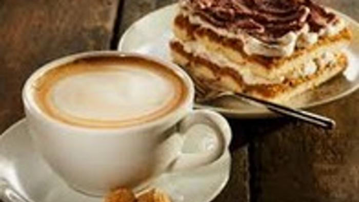 Kuchengedeck mit Kuchenstück auf einem Teller und einer Tasse Cappucchino daneben