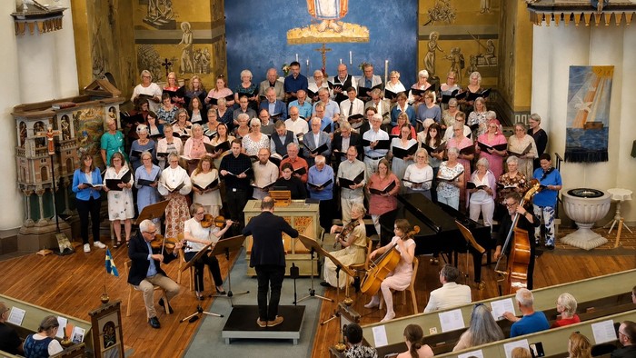 Ein großer Chor und Musiker treten gemeinsam in einer prächtigen Kirche mit vielen Besuchern auf.