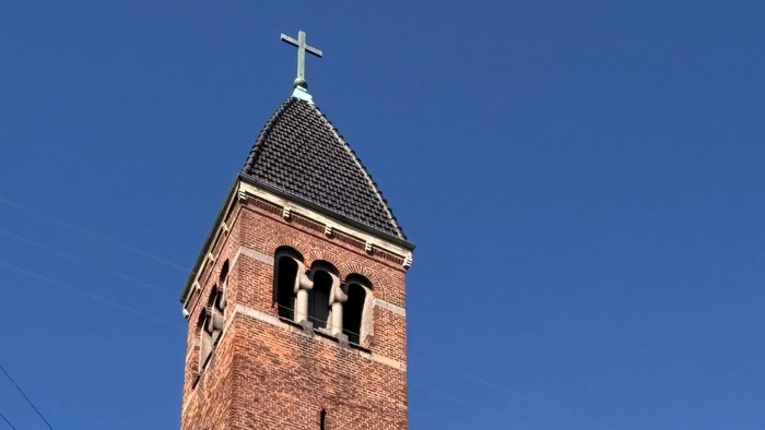 En historisk murstenskirke med højt klokketårn og buet indgang under klar blå himmel.