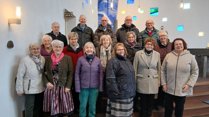 Gruppe älterer Menschen, die drinnen gemeinsam vor einer dekorierten Wand mit bunten Lichtern posieren.