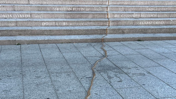 Ein rissiger Gehweg mit eingravierten lateinischen Namen auf einer Treppenanlage darüber.