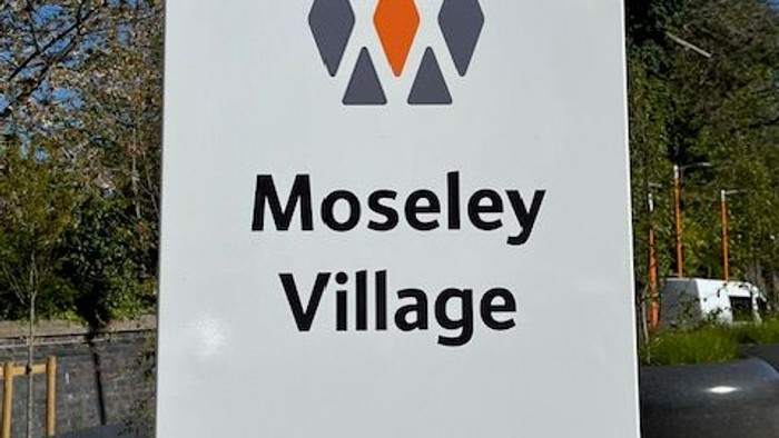 Signpost marking Moseley Village station with Network Rail and local council logos.