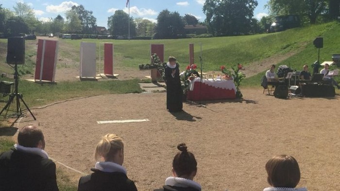 En gruppe af mennesker deltager i en udeaktivitet på en grøn area med redder og kameraer.
