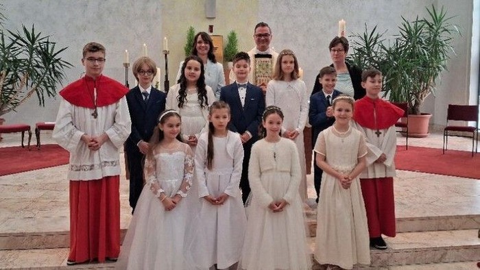 Gruppe von Kindern in formeller Kleidung, darunter Ministranten und Brautjungfern, die in einer Kirche posieren.