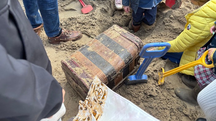 Kinder, die eine vergrabene Holzkiste in einem Sandkasten mit kleinen Schaufeln und Werkzeugen ausgraben.