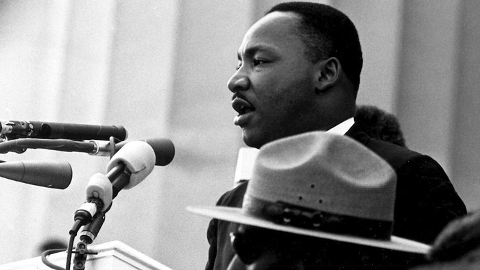 Ein Redner (Martin Luther King) vor Mikrofonen. Vor ihm ein Mann in Uniform.