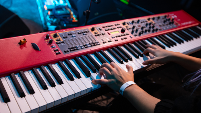Das Bild zeigt ein digitales Piano mit zwei Händen, die darauf spielen.