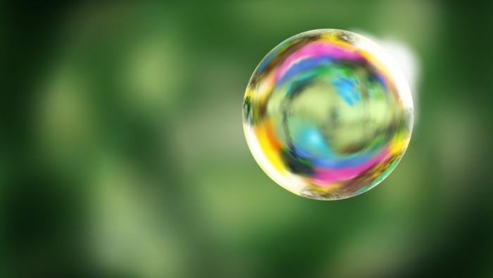 Eine schimmernde Seifenblase fängt lebendige Regenbogenfarben vor einem verschwommenen grünen Hintergrund ein.