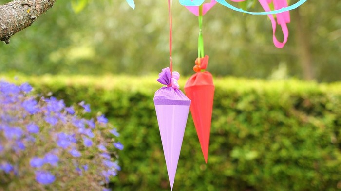Bunte Papierschmuckstücke hängen von einem Baumast.