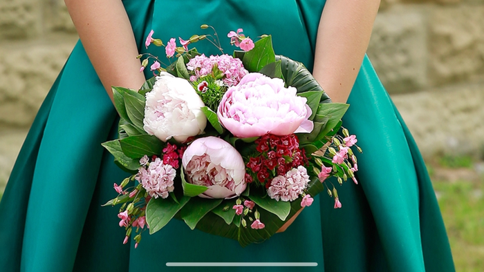 Eine Person in einem grünen Kleid hält einen Blumenstrauß mit rosa und weißen Blumen.